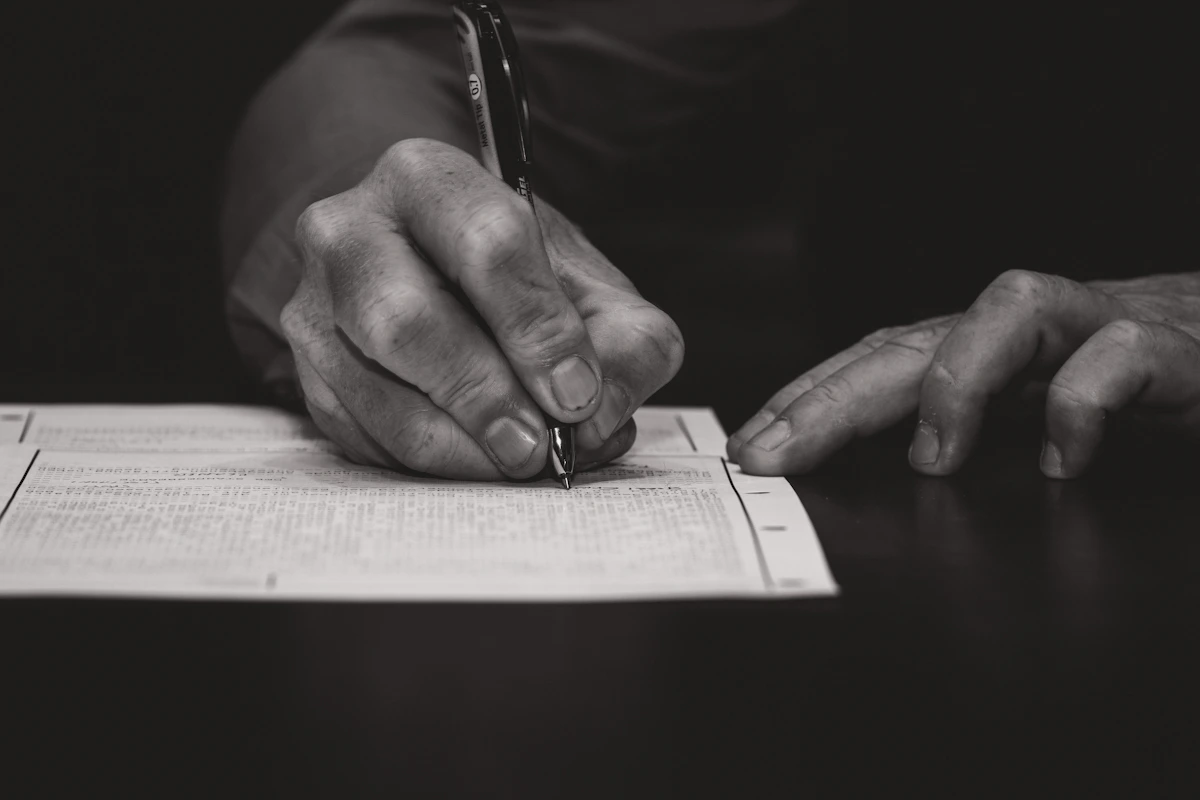 Manos escribiendo a pluma sobre un documento en la mesa del despacho.